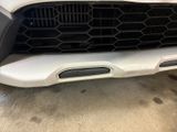 the front end of a white car with a grille and a number plate on it