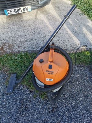 an orange and black vacuum cleaner sitting on top of a sidewalk next to a car