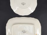 two white plates with gold trims on them on a black surface