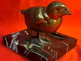 sculpture en bronze représentant un oiseau, posée sur un socle en marbre, sur fond rouge