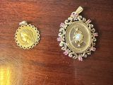 two gold pendants on a wooden table with pink stones