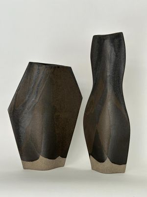 deux vases noirs posés l'un à côté de l'autre sur une surface blanche