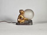 une statue représentant un garçon tenant un ballon, assis sur un rocher
