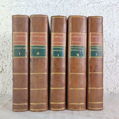 five old books are lined up on a shelf against a white wall