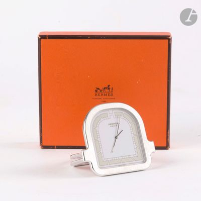 une horloge en argent posée devant une boîte orange