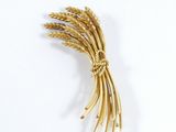 a gold brooch of wheat on a white surface