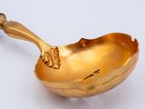 a gold spoon with a handle on a white surface