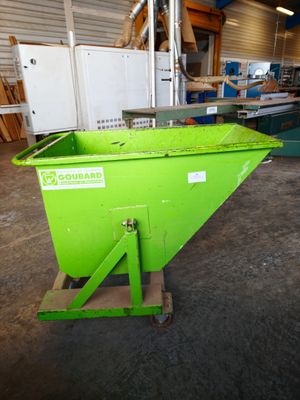 the green dumpster is sitting in the warehouse next to the other green bins