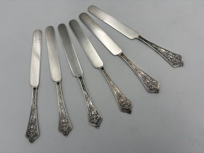 six silverplated knives and a knife on a white surface