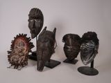 plusieurs masques africains posés sur des socles, sur une surface blanche