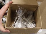 a person holding a cardboard box full of empty wine glasses