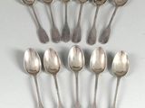 six cuillères en argent sont disposées en ligne sur une surface blanche