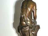 bronze statue of a woman sitting on a rock with her back to the camera
