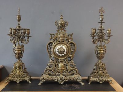 three gold colored candlesticks and a clock on a table