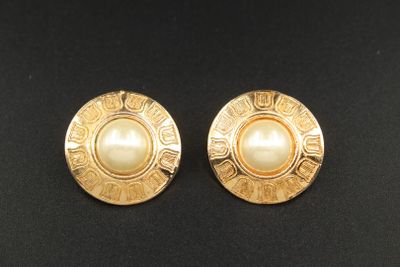 une paire de boucles d'oreilles en or et perles posées sur un fond noir