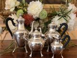 quatre théières en argent posées sur une table, avec des fleurs en arrière-plan