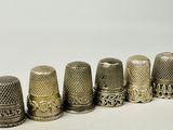six antique thimbles lined up in a row on a white surface