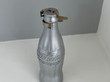 une bouteille de Coca-Cola argentée avec un bouchon doré, posée sur une table blanche
