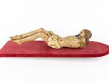 statue of a man laying on a red cushion on a white background