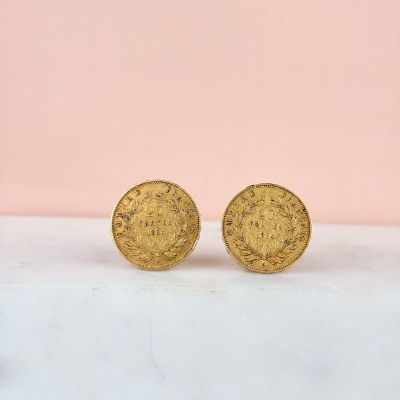 une paire de boucles d'oreilles en forme de pièces d'or posées sur un comptoir en marbre