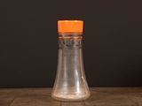 une petite bouteille en verre avec un bouchon orange posée sur une table
