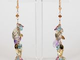 a pair of earrings with multi colored stones on a clear stand