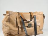 the large tan leather bag is sitting on a white surface