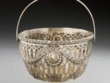 an antique silver basket with a handle on a white surface