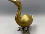 gold duck figurine on a white surface with a gray background