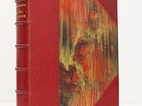 an old book with a red cover sitting on top of a white surface