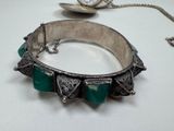 a silver bracelet with green stones on it and a pocket watch in the background
