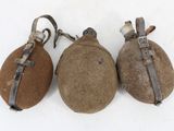 three old, rusty, and worn flasks sitting on a white surface