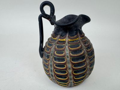 un vase noir et jaune muni d'une anse, posé sur une table blanche