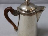 an antique silver coffee pot with a wooden handle on a white surface