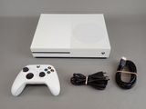 the white xbox one is sitting next to a charger and a cable