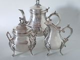 three silver teapots and a coffee pot sitting on a table