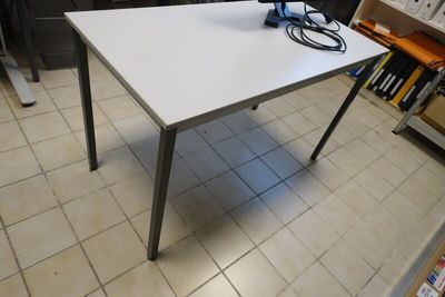 une table blanche sur laquelle est posé un ordinateur portable, dans une pièce