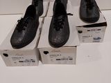 trois paires de chaussures noires posées sur des cartons