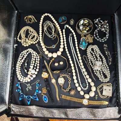 une valise ouverte, remplie de nombreux bijoux, posée sur un parquet