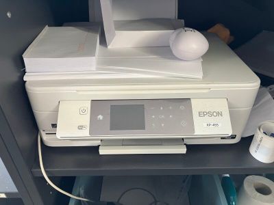 une imprimante posée sur une étagère, à côté d'un rouleau de papier toilette