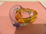 un objet en verre en forme de cœur posé sur une surface rose