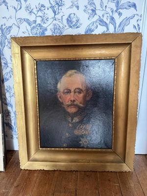 tableau représentant un homme moustachu, dans un cadre doré, posé sur un plancher en bois