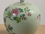 a green vase with flowers on it sitting on a table