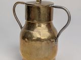 an antique brass pitcher with a handle on a white background