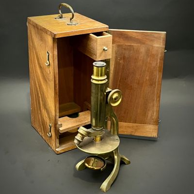un vieux microscope en laiton avec un coffret en bois sur fond gris