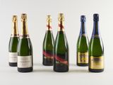 six bottles of champagne lined up in a row on a white surface