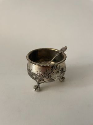 an old silver bowl with a spoon sitting on top of it