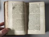 someone is holding an open book in their hand on a table