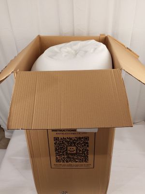 une boîte en carton contenant un oreiller, posée sur un lit