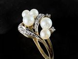a close up of a ring with pearls and diamonds on a black surface